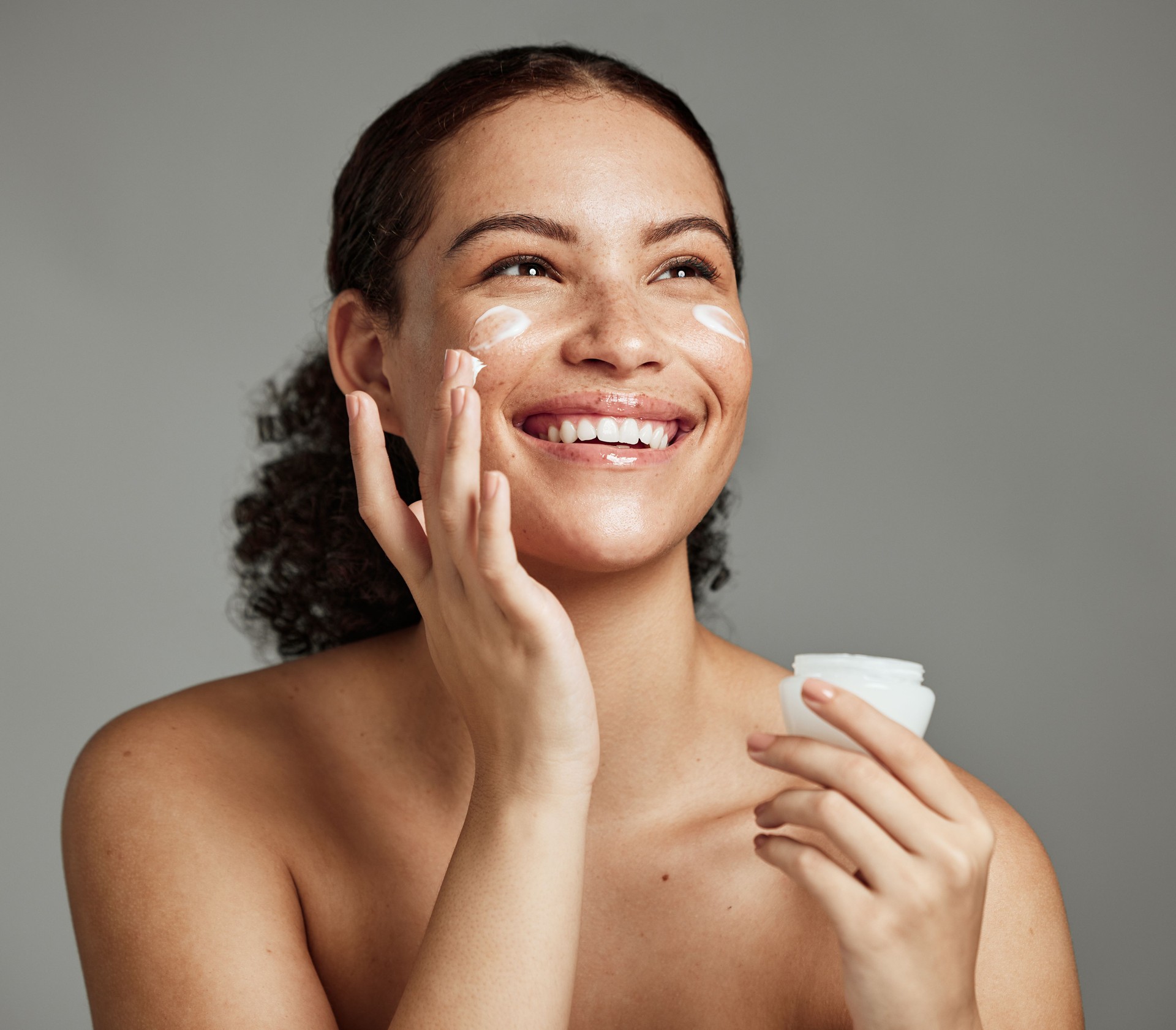 Black woman, smile and face beauty cream for skincare wellness shine, cosmetics dermatology and salon spa product in studio. African girl, spf lotion and self care happiness for luxury facial glow